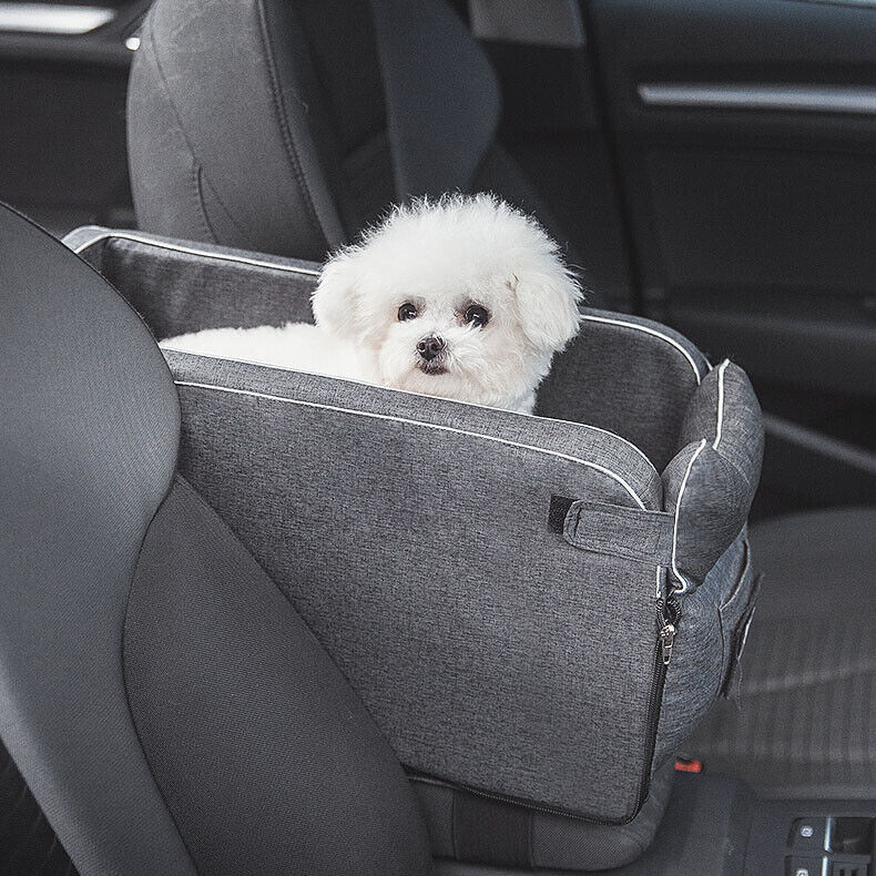 White fluffy dog sitting in a grey console pet car seat on a vehicle passenger seat